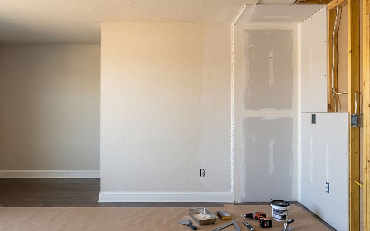 Open stud framing on one side of a room and finished, taped and painted drywall on the other