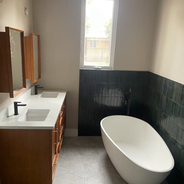 Completed bathroom with a freestanding bath, dark tiled wainscot and a timber vanity