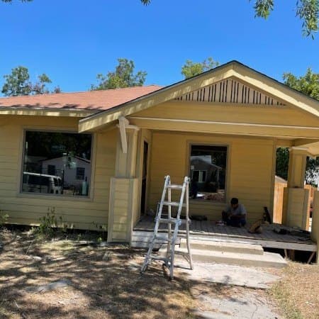 Yellow clapboard house exterior with a covered porch and a ladder set up