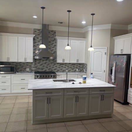 Finished kitchen with a grey island, white cabinets, extractor hood and pendant lights