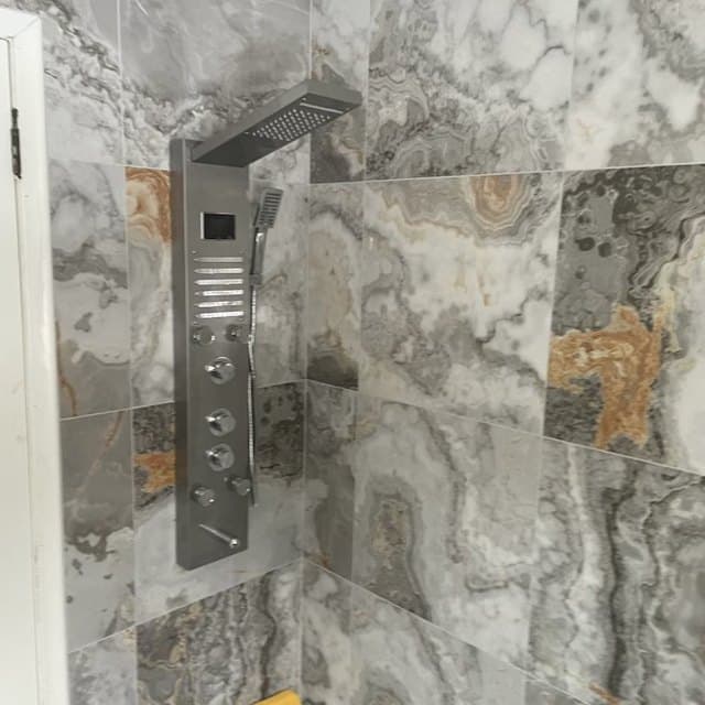 Walk in shower lined floor to ceiling in marble effect tile with a built in niche